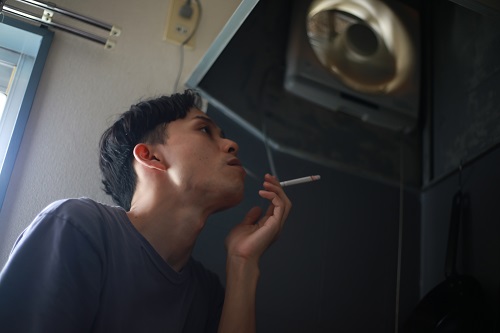 換気扇の下でタバコを吸う男性